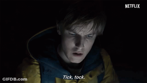 Man In Yellow Jacket Says Tick Tock In Dark Room GIF