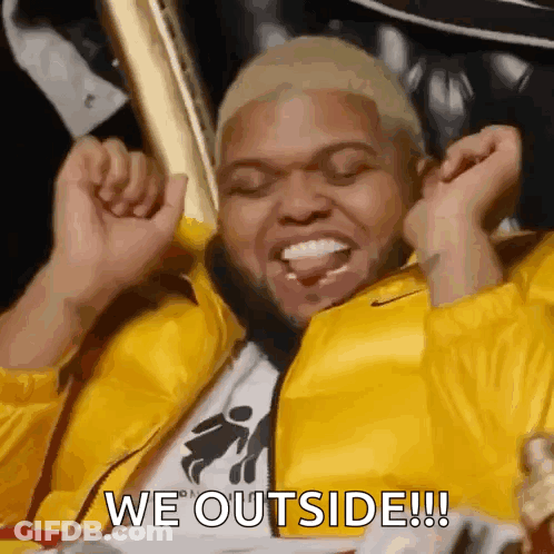 Man In Yellow Jacket Sitting With Arms Up GIF