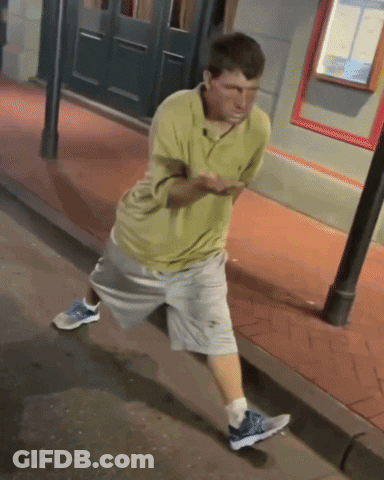 Man In Yellow Shirt And Grey Shorts On Sidewalk GIF