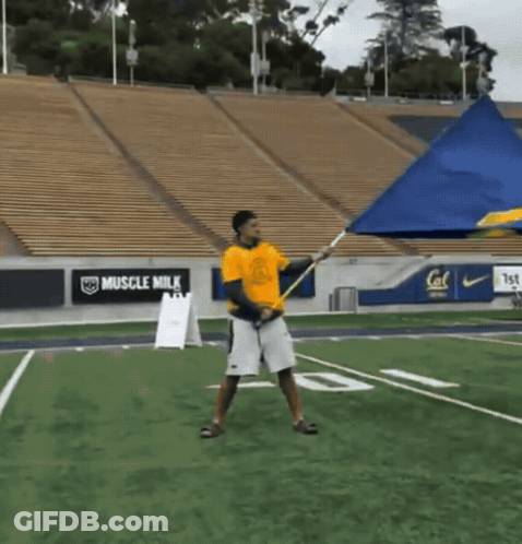 Man In Yellow Shirt Holding Flag With Muscle Milk Ads GIF