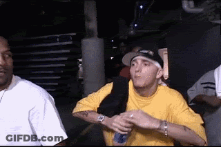 Man In Yellow Shirt Holding Microphone Next To Man In Black Hat GIF