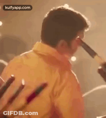 Man In Yellow Shirt Holding Sticks GIF