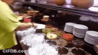 Man In Yellow Shirt In Front Of Cakes And Plates GIF
