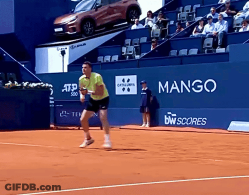Man In Yellow Shirt Playing Tennis In Front Of Mango Sign GIF