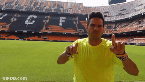 Man In Yellow Shirt Pointing At Stadium GIF