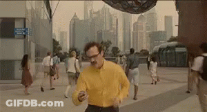 Man In Yellow Shirt Running Looking At Cell Phone GIF