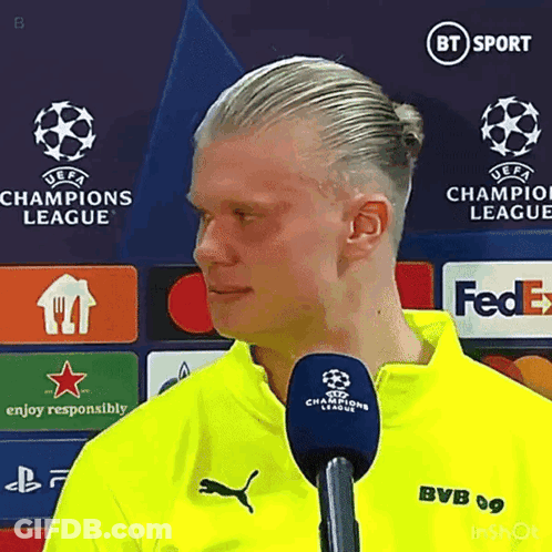 Man In Yellow Shirt Talking Into Microphone In Front Of Champions League Sign GIF