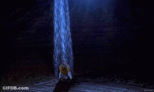 Man In Yellow Shirt Under Waterfall In Dark Room GIF
