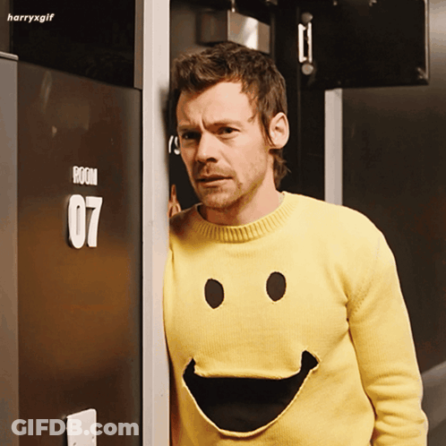 Man In Yellow Smiley Sweater In Front Of Room 07 Door GIF