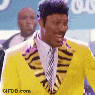 Man In Yellow Suit And Tie Smiling In Front Of Crowd GIF
