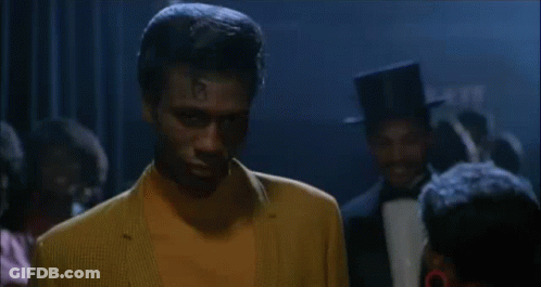 Man In Yellow Suit Standing With Group In Dark Room GIF