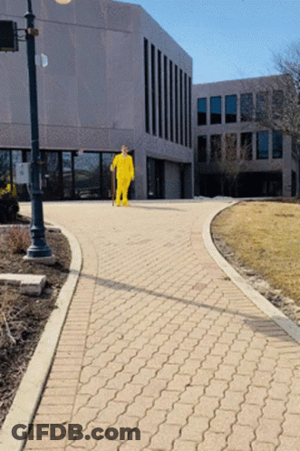 Man In Yellow Suit Walking Down Brick Walkway GIF
