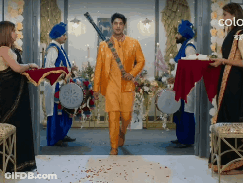 Man In Yellow Suit Walking Through Doorway Surrounded By Blue Turbans GIF
