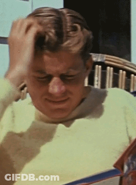 Man In Yellow Sweater Scratching Head Reading Magazine GIF