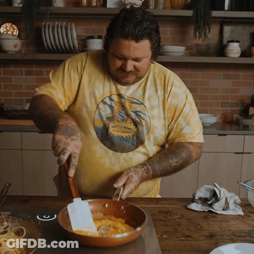 Man In Yellow Tie Dye Shirt Stirring Skillet GIF