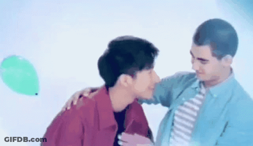Man Kissing Another Man On Cheek With Green Balloon GIF