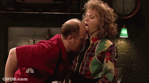 Man Kissing Woman On Cheek In Front Of Clock 2:01 GIF