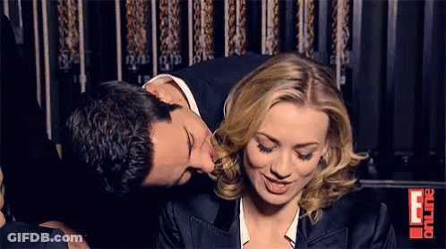 Man Kissing Woman On Cheek In Front Of E Sign GIF