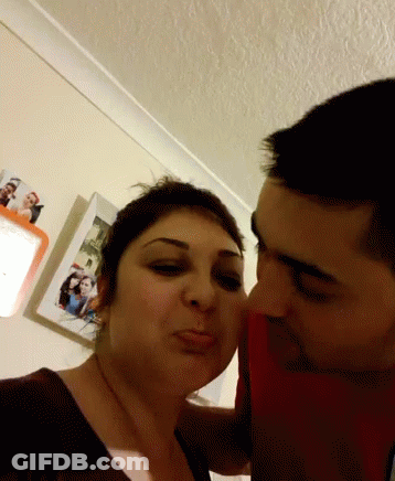 Man Kissing Woman On Cheek In Front Of Pictures GIF