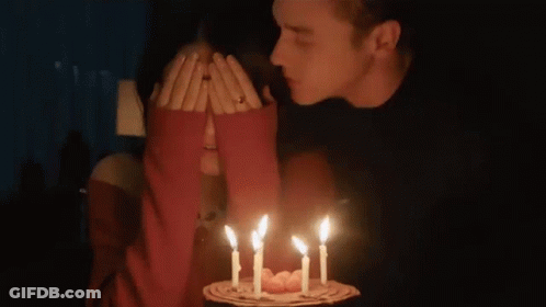 Man Kissing Woman's Cheek Lit Birthday Cake Candles GIF