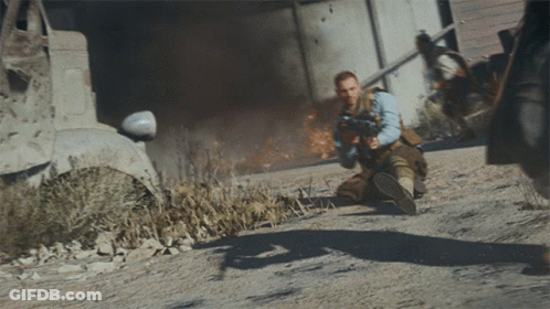 Man Kneeling Holding Gun Before Burning Building GIF