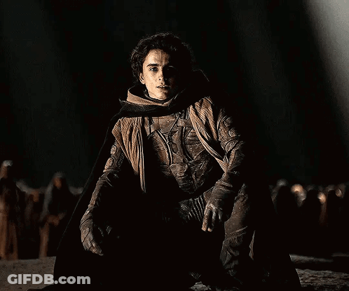 Man Kneeling In Dark Wearing Cape GIF