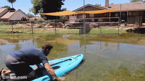 Man Kneeling On Blue Kayak In Flooded Area GIF