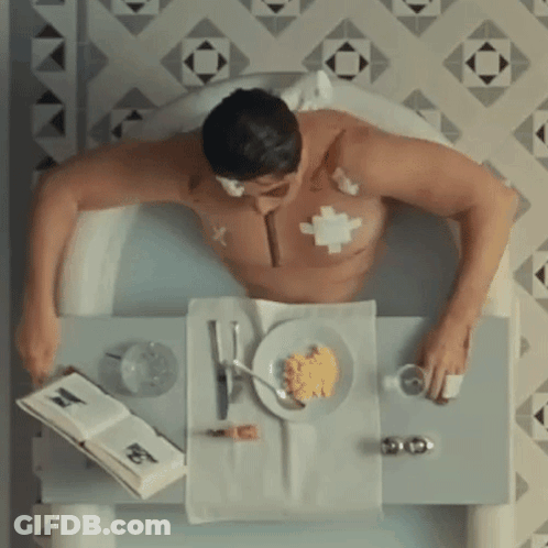 Man Laying In Bathtub With Food And Book GIF