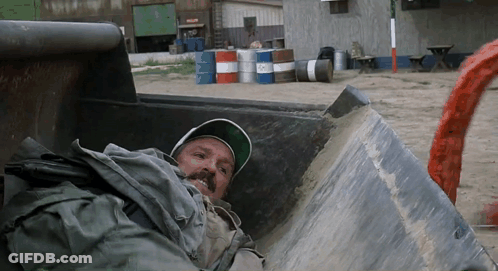 Man Laying In Dumpster With Barrels GIF