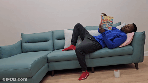 Man Laying On Blue Couch Reading Bobs GIF