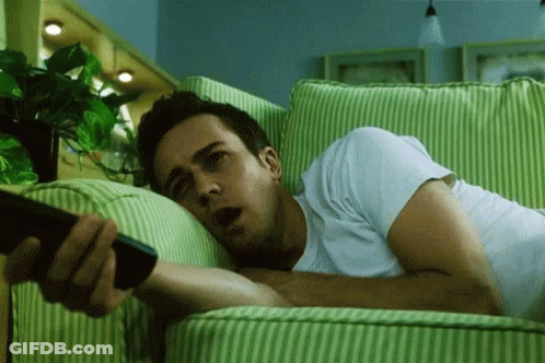 Man Laying On Green And White Striped Couch Holding Remote GIF