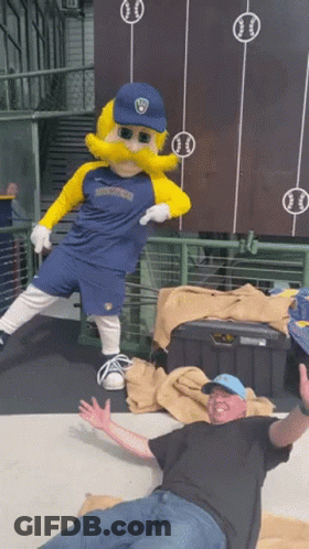 Man Laying On Ground Next To Mascot In Brewers Jersey GIF
