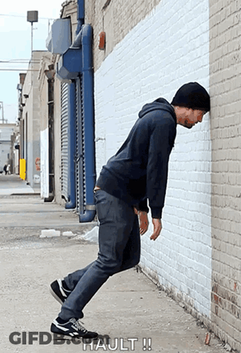 Man Leaning Against Brick Wall Saying Hault GIF