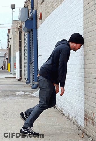 Man Leaning Against White Brick Wall In Alleyway GIF