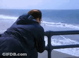 Man Leaning Over Railing Looking Out Over Ocean GIF
