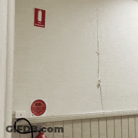 Man Looking Through Hole In Wall With Red Sign Saying Co GIF