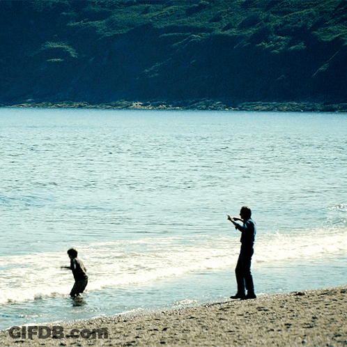 Man On Beach Watching Boy In Water GIF