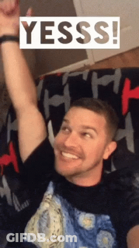 Man On Couch With Arm Up Saying Yesss GIF