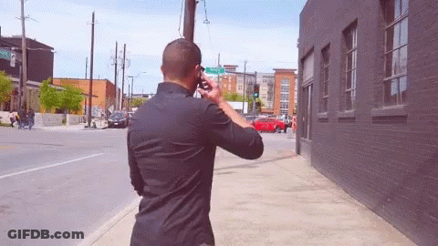 Man On Phone Walking By Green Street Sign GIF