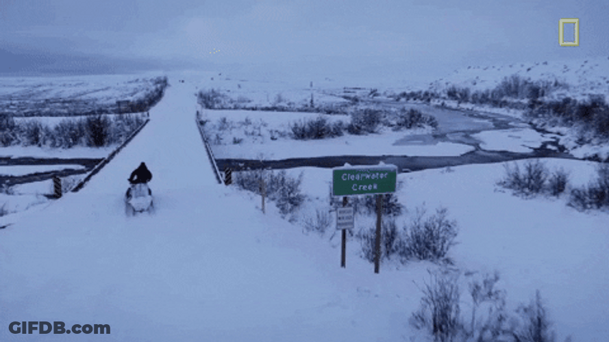 Man On Snowmobile Crossing Snowy Bridge GIF