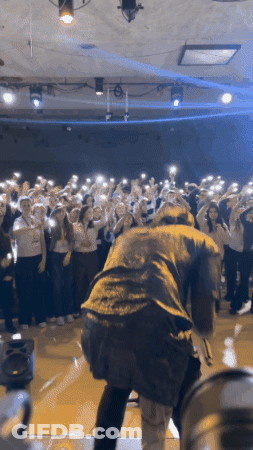 Man On Stage In Front Of Crowd Holding Up Phones GIF