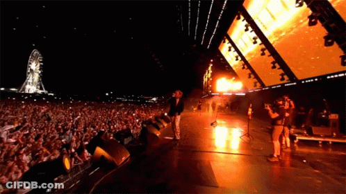 Man On Stage In Front Of Ferris Wheel GIF