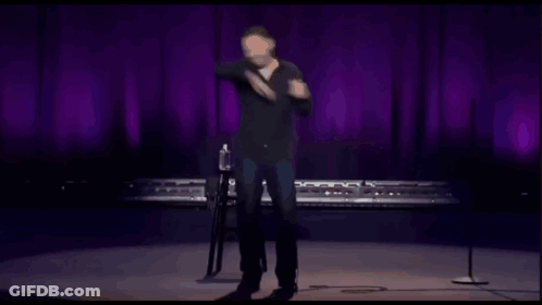 Man On Stage With Microphone In Front Of Purple Curtain GIF