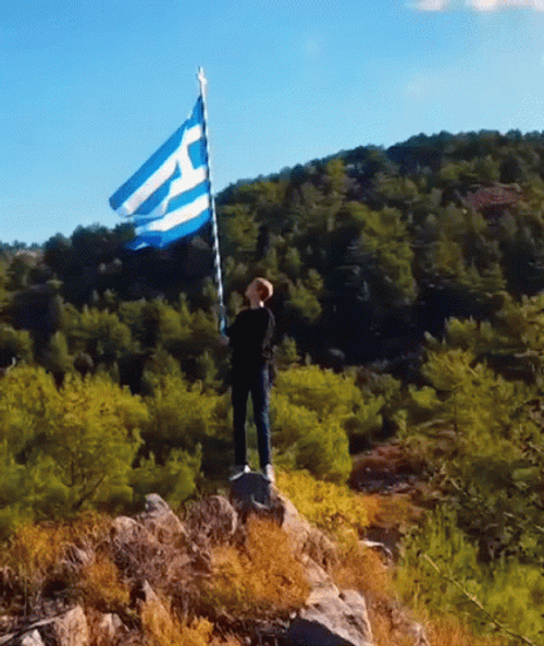 Man On Top Of Mountain Lifting Greece Flag GIF