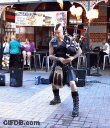 Man Playing Bagpipes In Front Of Scottish Sign GIF
