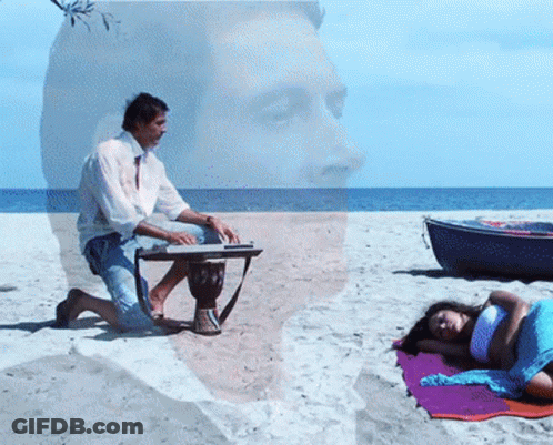 Man Playing Drum On Beach With Woman Laying On Towel GIF