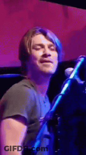 Man Playing Flute In Front Of Bob Mills Sign GIF