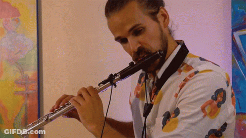 Man Playing Flute In Front Of Colorful Painting GIF