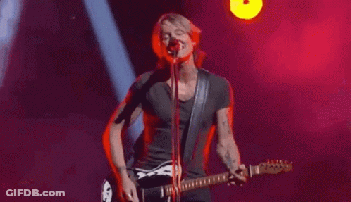 Man Playing Guitar And Singing Into Microphone On Stage GIF