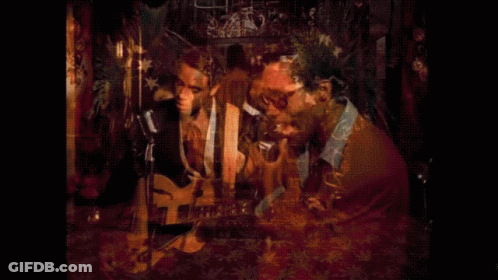 Man Playing Guitar And Singing Into Microphone While Another Man Looks On GIF